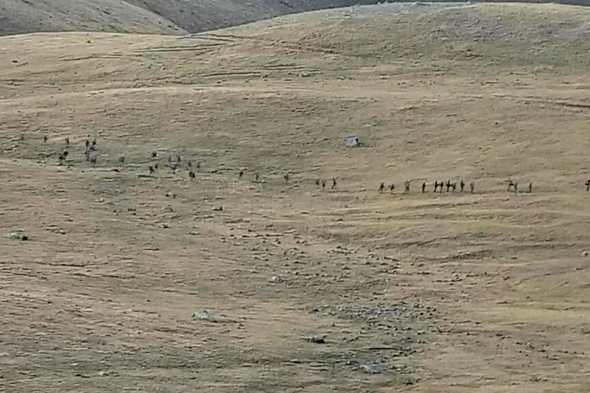 Picture from a distance of soldiers marching in an open area 