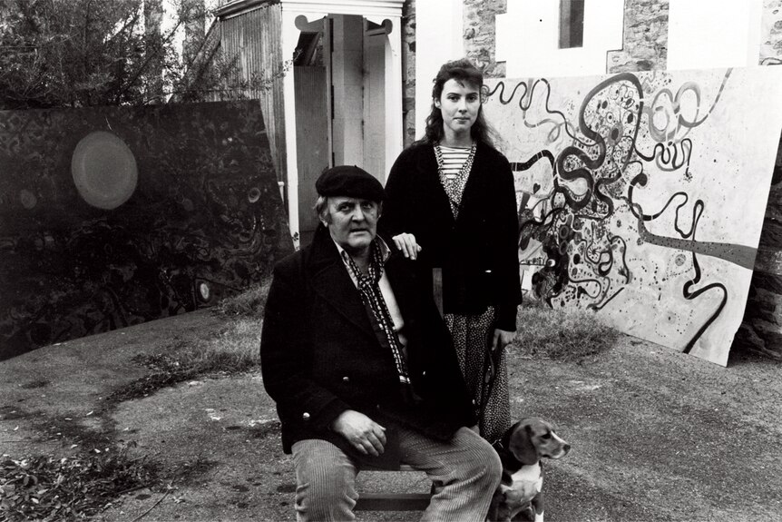 Black and white portrait of a man in a beret seated his teenage daughter standing