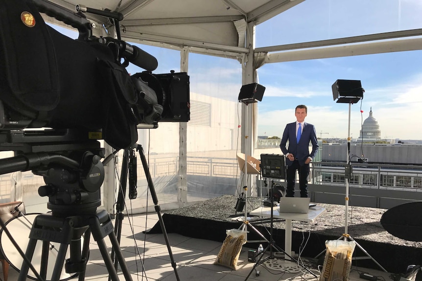 Rowland standing in front of cameras and lights with Capitol building in the background.