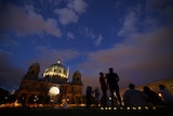 People socialise in the early evening in front of a large, dimly lit cathedral in Berlin.