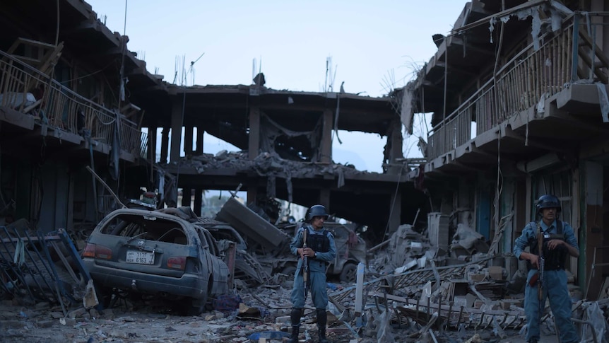 Afghan policemen stand guard at a market destroyed by a powerful truck bomb in Kabul