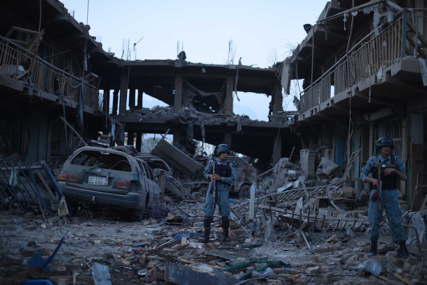 Afghan policemen stand guard at a market destroyed by a powerful truck bomb in Kabul