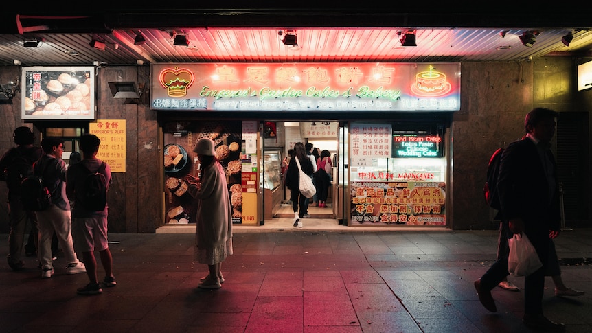 在中餐馆招牌的霓虹灯下，人们聚集在昏暗的人行道上。