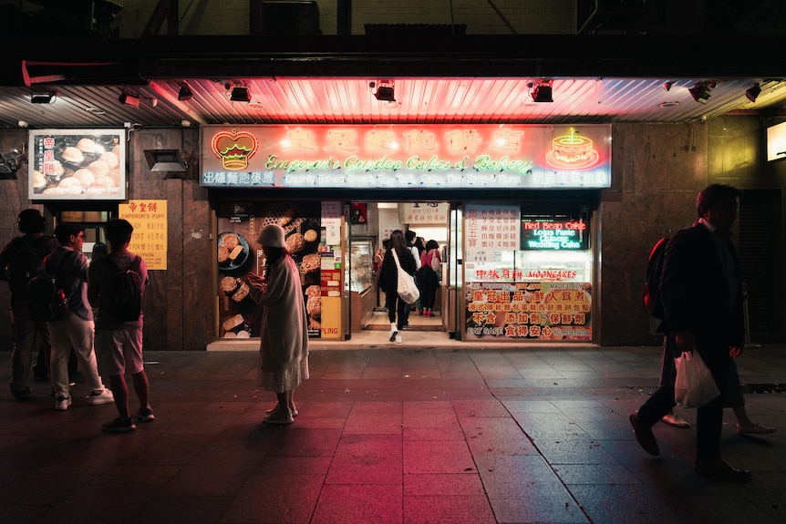 People gather on a dark pavement under the neon glow of Chinese restaurant signs.