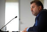 Ange Postecoglou in profile with a microphone in front of him.