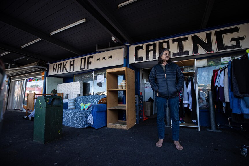 Debbie stands with no shoes in front of the signage: 'Waka of Caring'