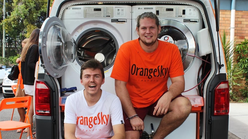 Two men sit on a truck with washing machines on it
