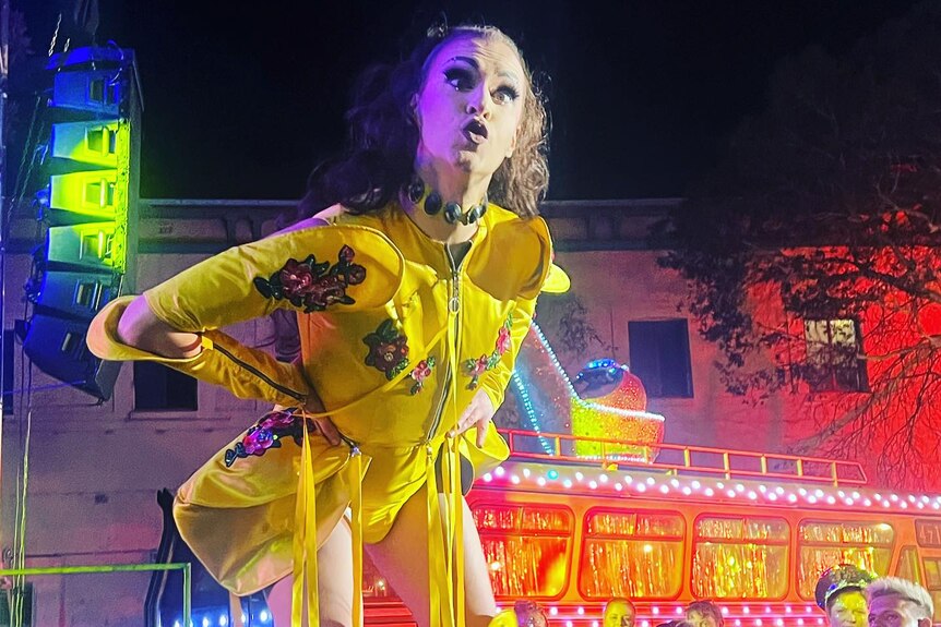 A drag queen wearing a brightly coloured outfit on a brightly lit stage