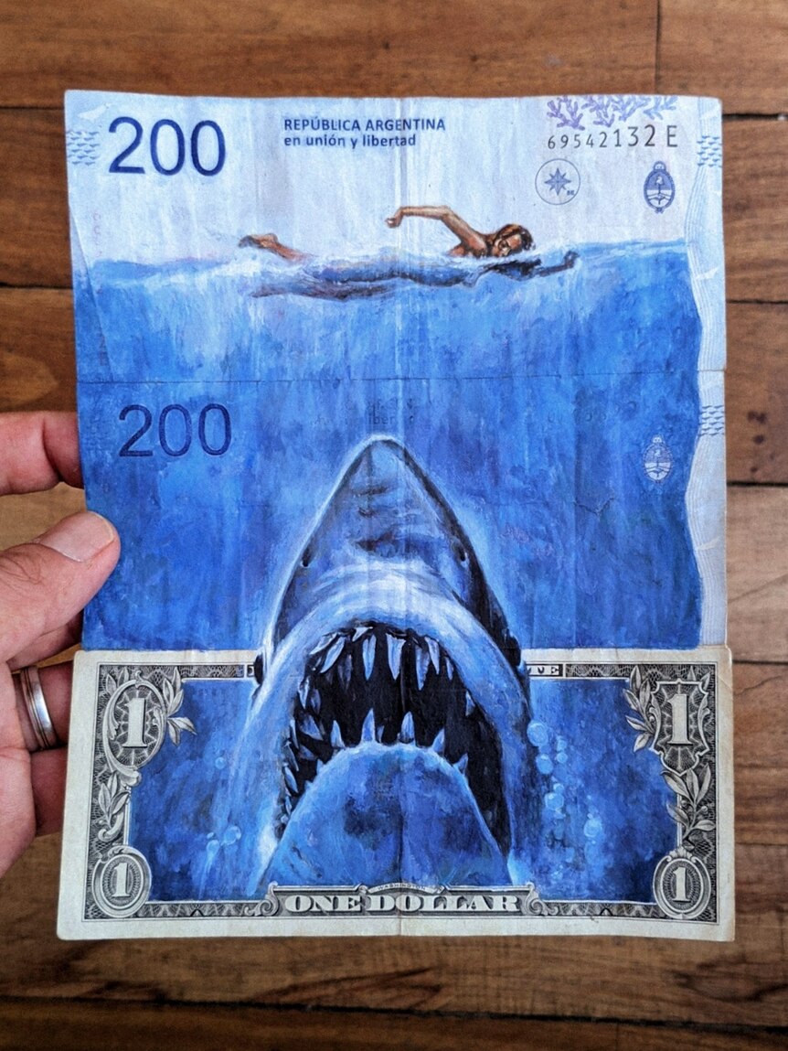 A shark is painted on a US dollar bill, hunting down a swimmer painted on a 200 peso note.