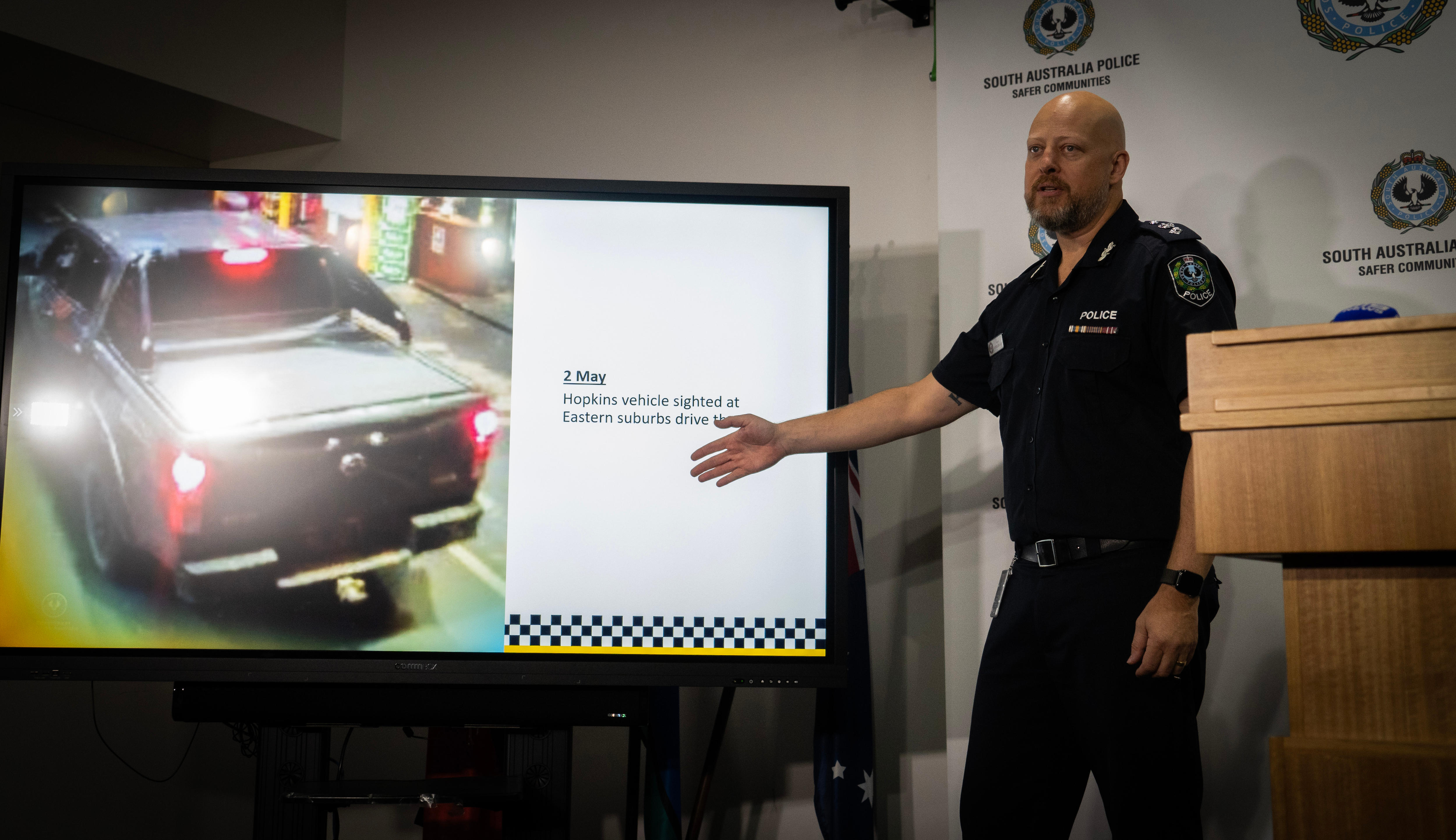 A police officer points to a display picture of a ute pulled up in a bottleshop drive thru.