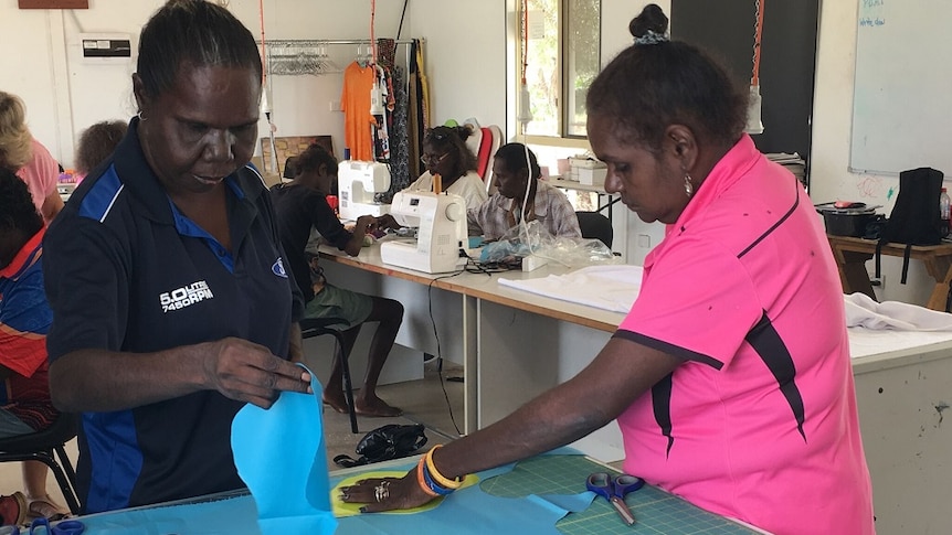 Two Doomadgee women cut out blue material to create the washable sanitary pads.