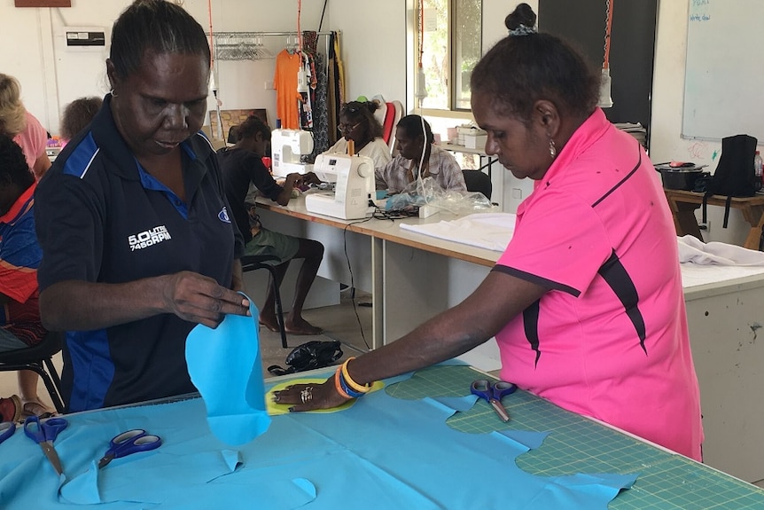 Two Doomadgee women cut out blue material to create the washable sanitary pads.