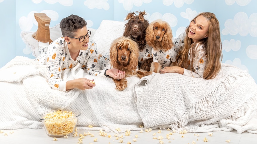 Lauren and Naomi in a stylised photoshoot in their PJs and on a bed with their three dogs