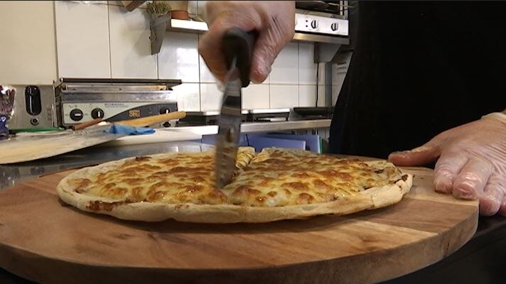 A pizza is cut with a rolling slicer while resting on a circular chopping board.