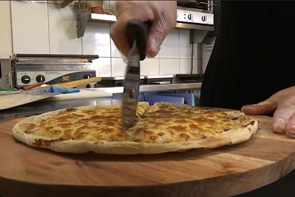 A pizza is cut with a rolling slicer while resting on a circular chopping board.