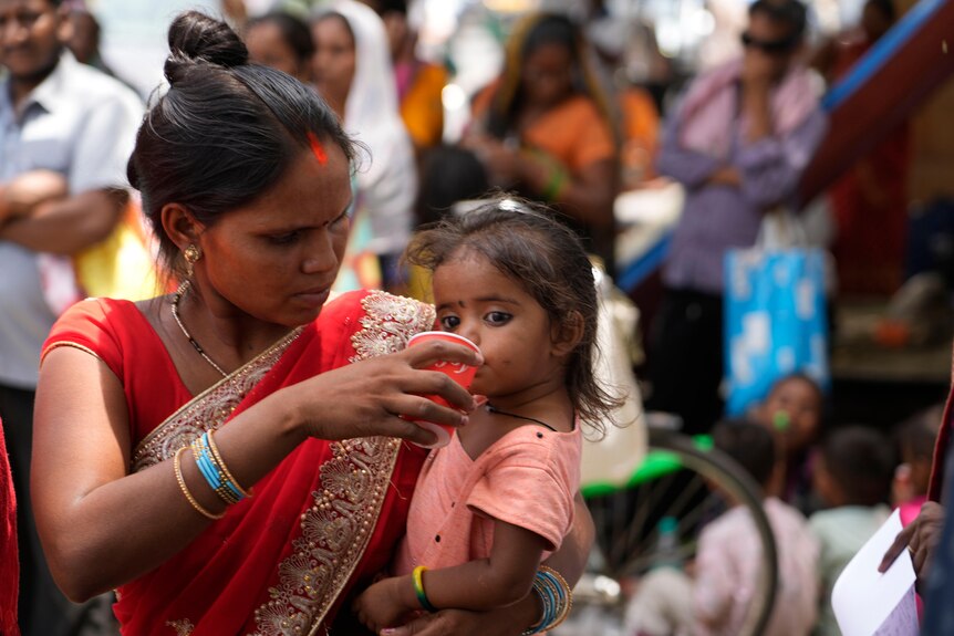 A woman gives a cold drink to her daughter in India.