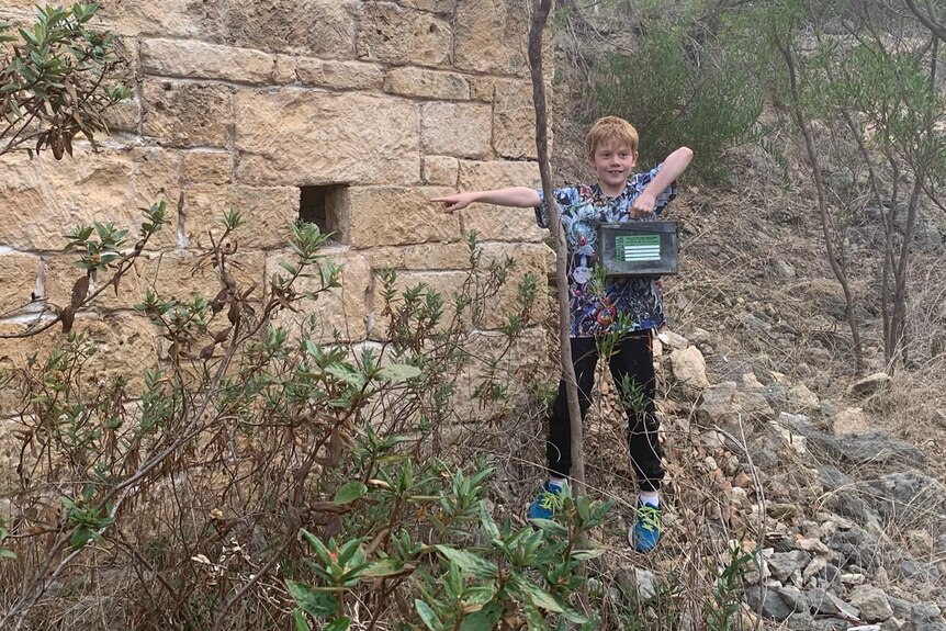 Boy points to a hole on a wall where he found a geocache. 