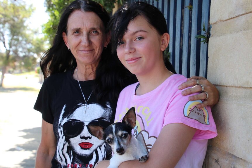 A woman with her arm around her daughter, who is holding a dog.