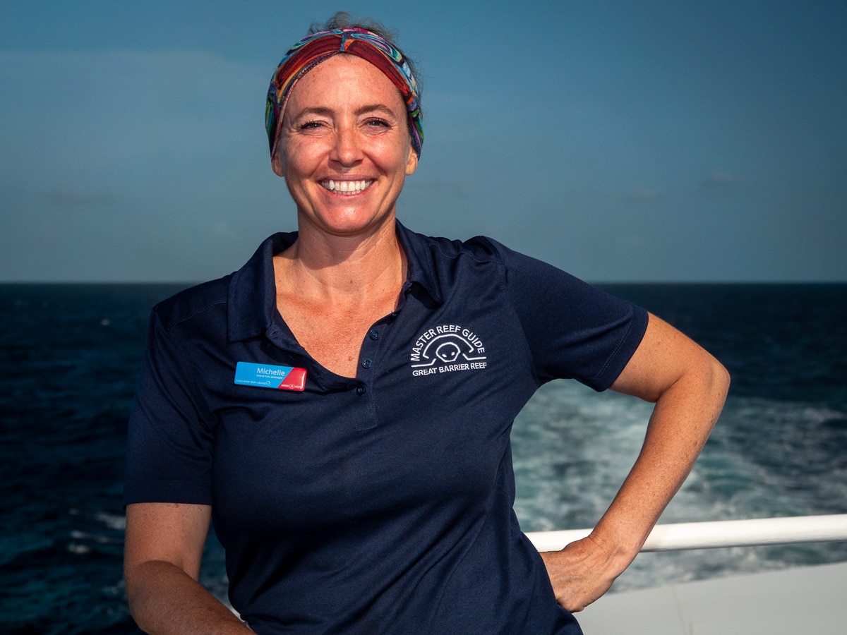 Una mujer sonriente con un pañuelo en la cabeza y un polo se encuentra en un barco en el mar.