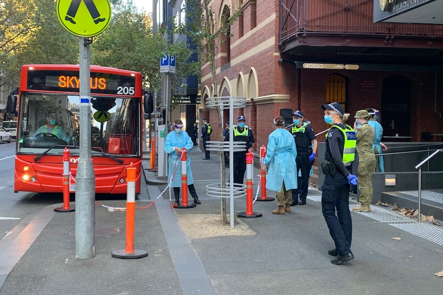 A red Skybus is parked in front of the hotel, as quarantine workers, police and army officers stand by.