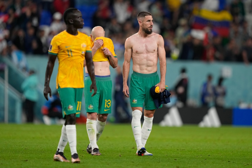 Milos Degenek walks on the field with his shirt off after the Socceroos lost their Qatar World Cup match against France.