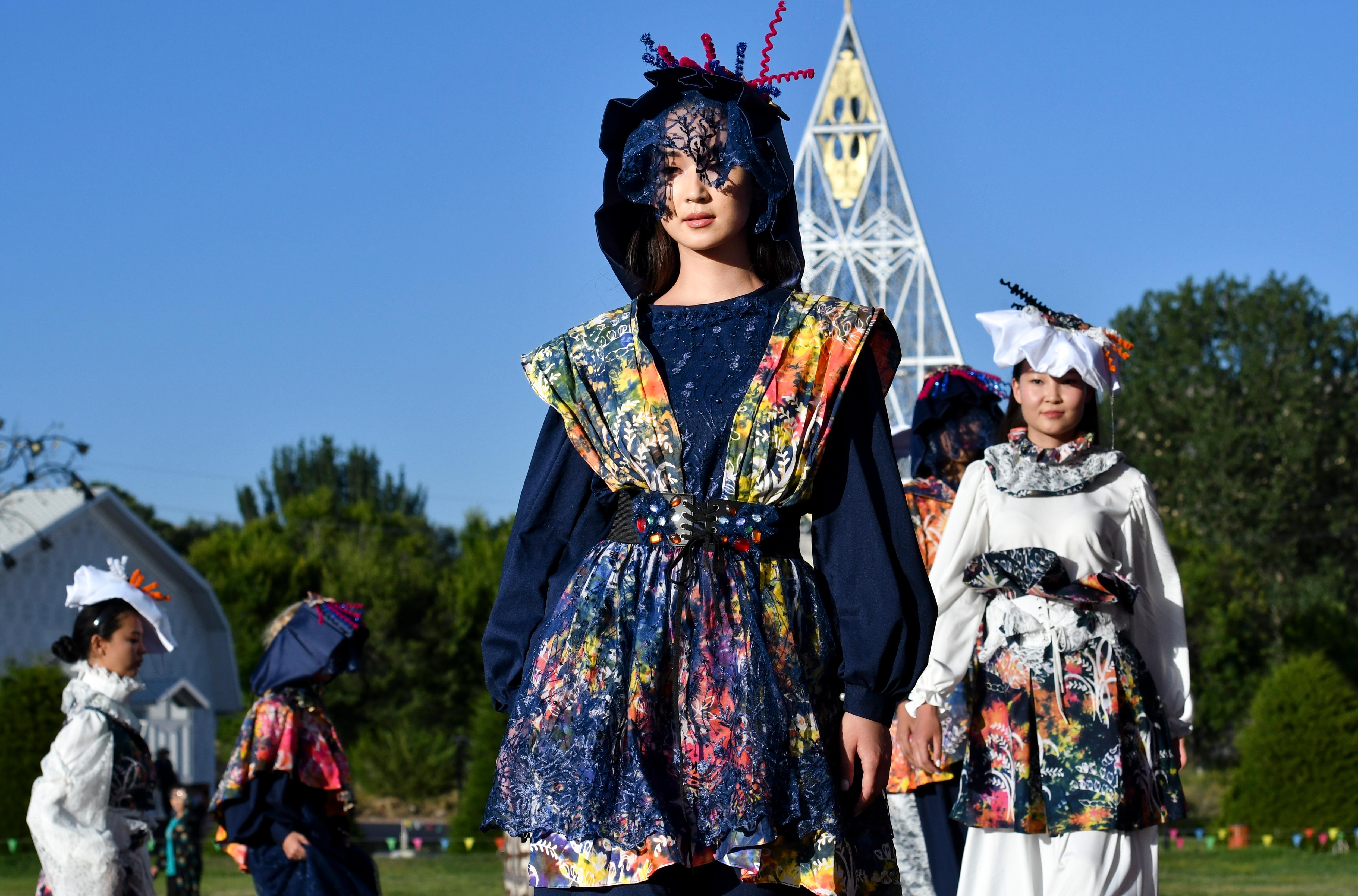 A model in a blue outfit walks down a runway, there are women behind her. 