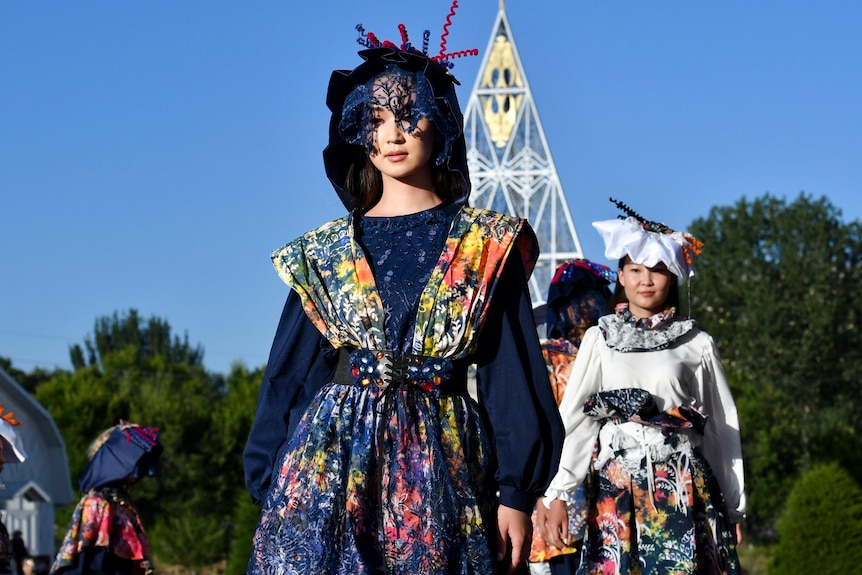 A model in a blue outfit walks down a runway, there are women behind her. 