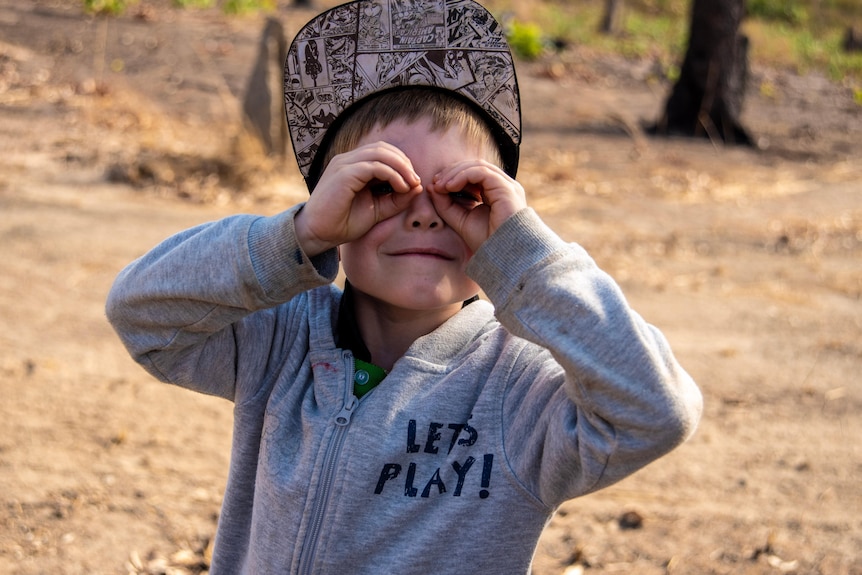 A young student looks at the camera with his hands forming the shape of binoculars. 