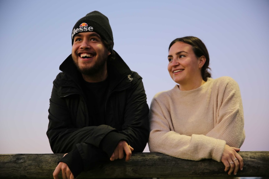 Trei and Karlie lean against a fence. They are smiling.