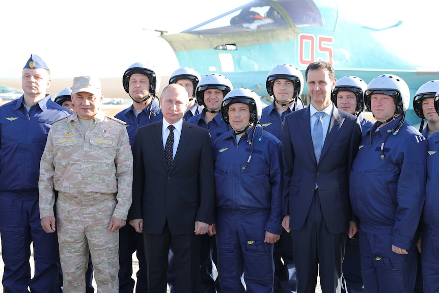 A group of politicians and air force officers pose in front of a jet fighter