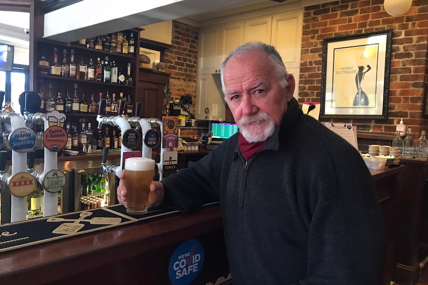 A man sits at the bar with a beer in hand
