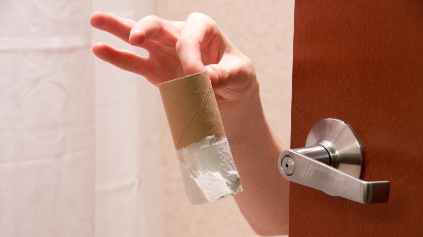 A person holding an empty toilet paper roll through a door