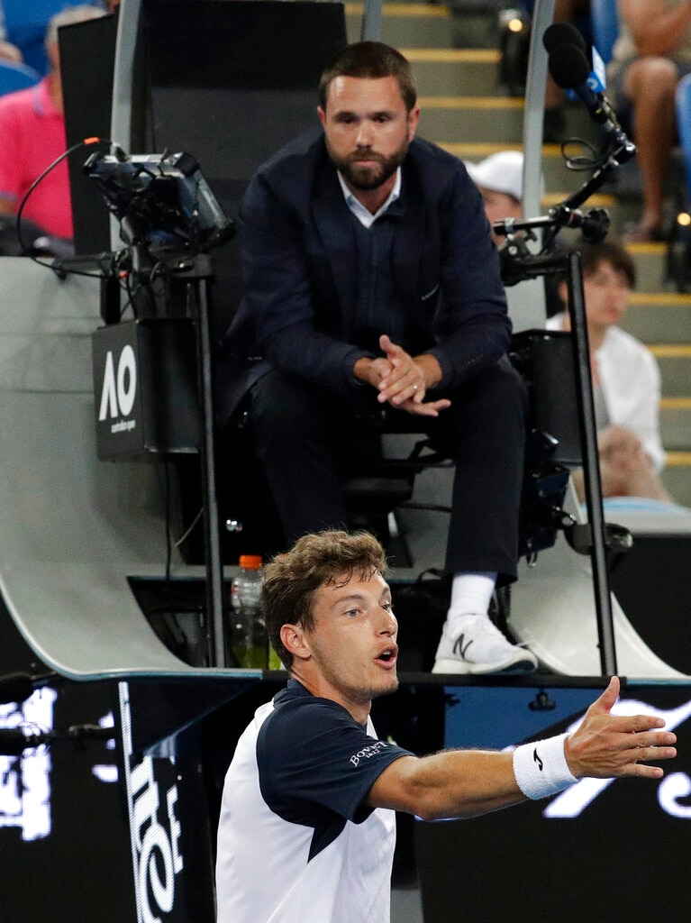 A tennis player gestures as he argues with a chair umpire sitting in a tall umpire chair