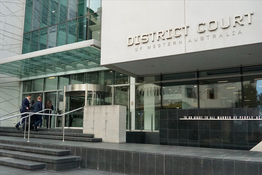 A wide shot of the District Court in Perth with two men walking towards its doors.