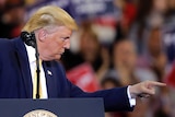 US President Donald Trump points to his left with a stern look on his face while standing at a lectern during a rally.