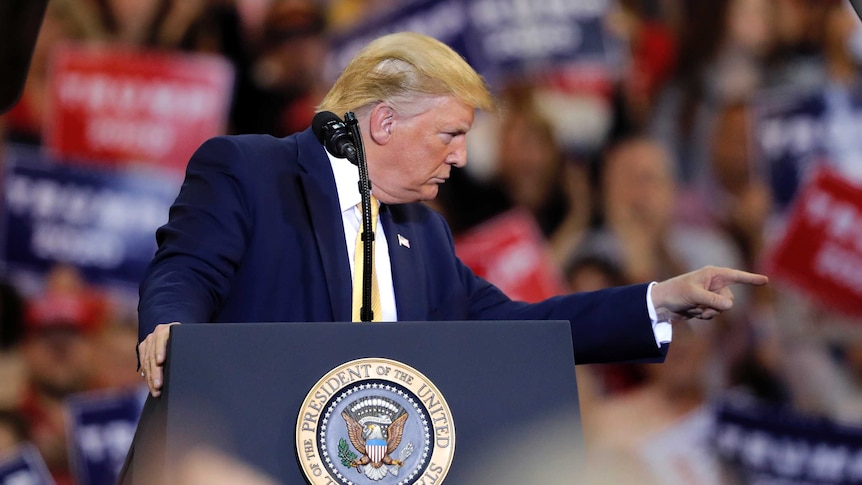 US President Donald Trump points to his left with a stern look on his face while standing at a lectern during a rally.