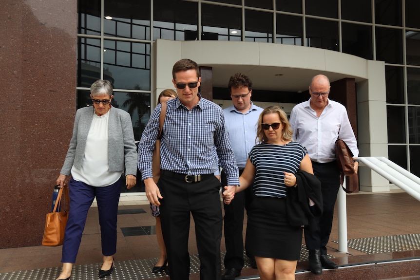 A group of people walk out of a courthouse building. A man in the front holds hands with a woman. 