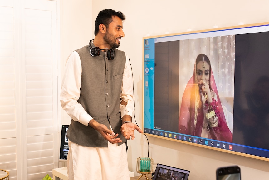 Groom, Athar Ali, at his home looks at his bride, Hani Ali, on TV screen.