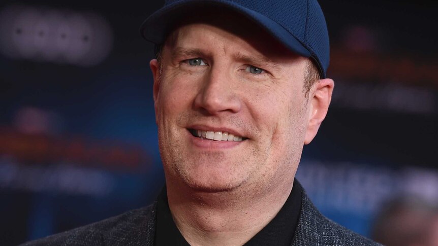 A man wearing a dark navy hat and grey suit jacket with black shirt.
