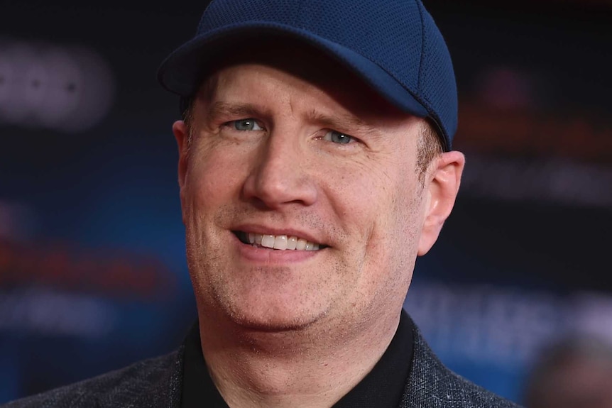 A man wearing a dark navy hat and grey suit jacket with black shirt.