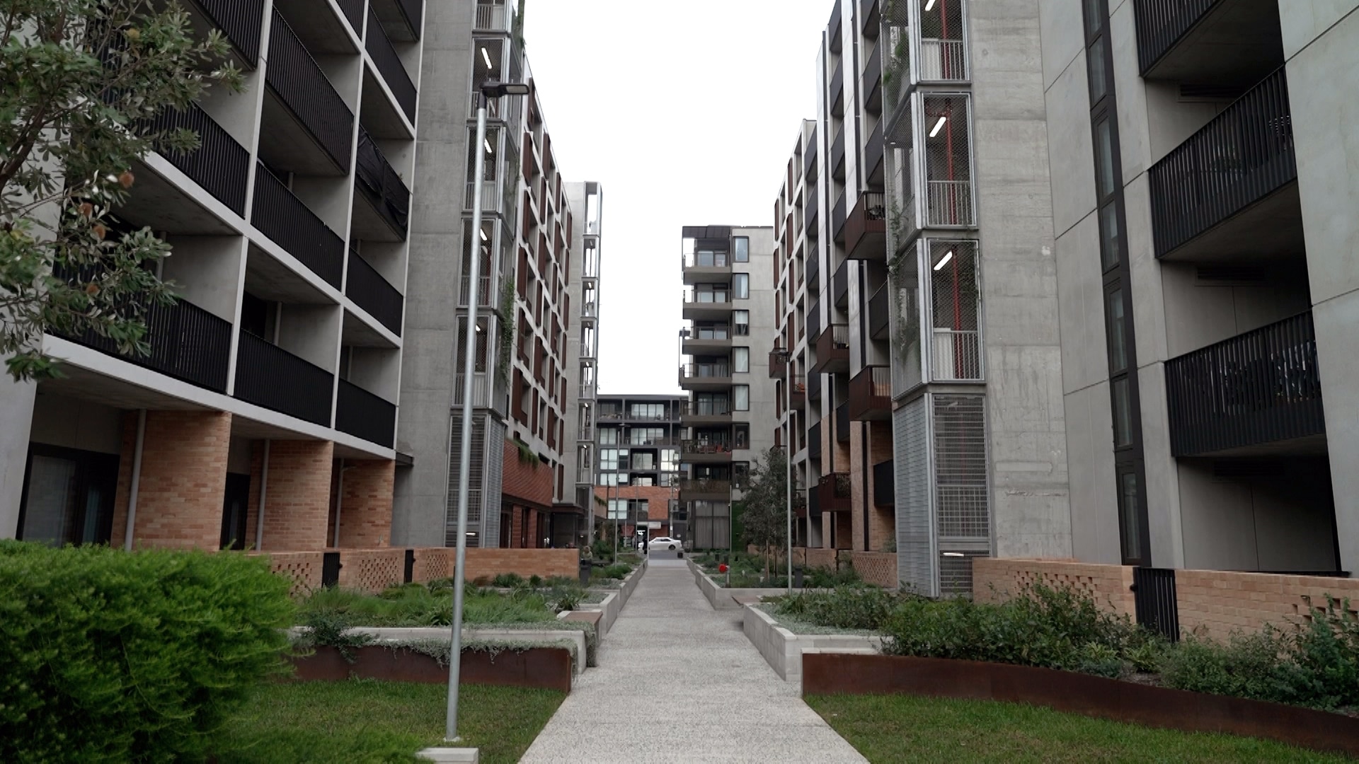 A walkway divides two large modern multi-storey apartment buildings.
