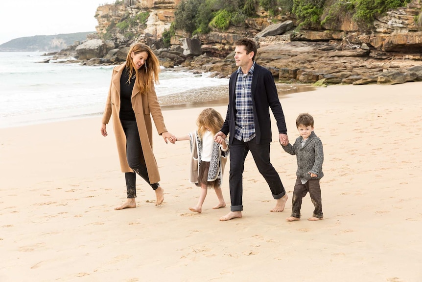 Two parents walk along a beach arm in arm with two small children on a winter's day.