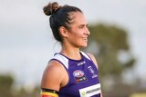 An young indigenous woman wearing a purple single and shorts, looks into the distance smiling
