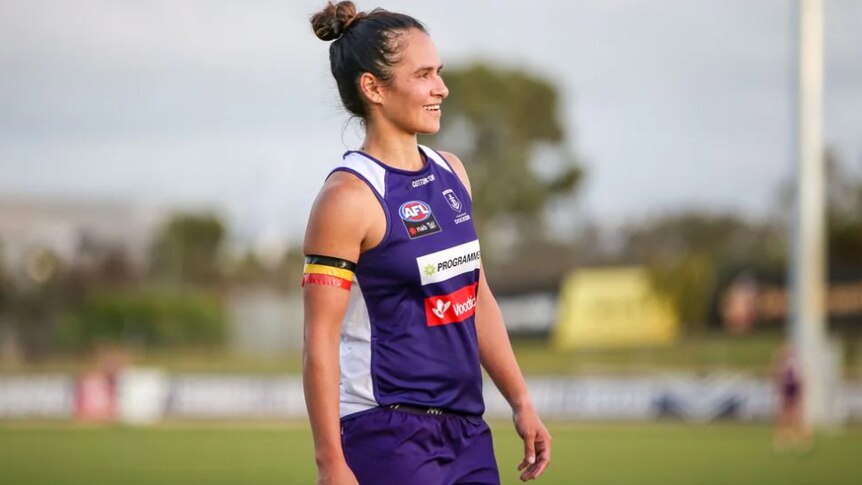 An young indigenous woman wearing a purple single and shorts, looks into the distance smiling