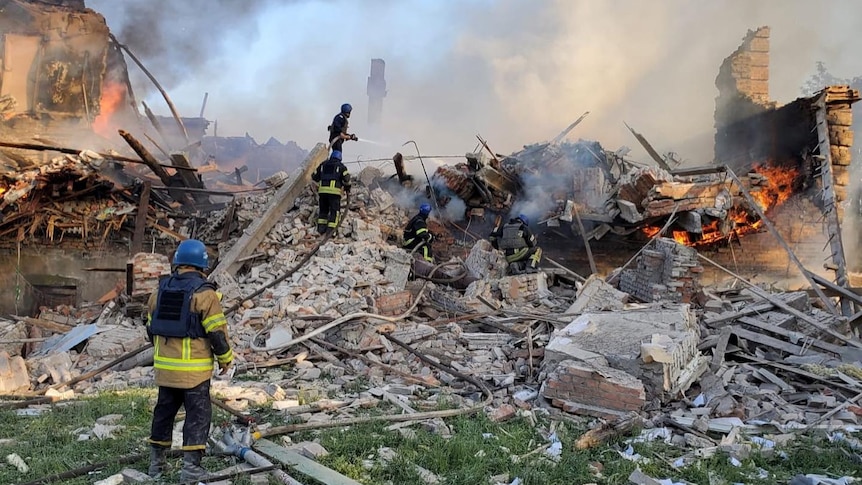 Emergency crew work on top of smouldering debris.