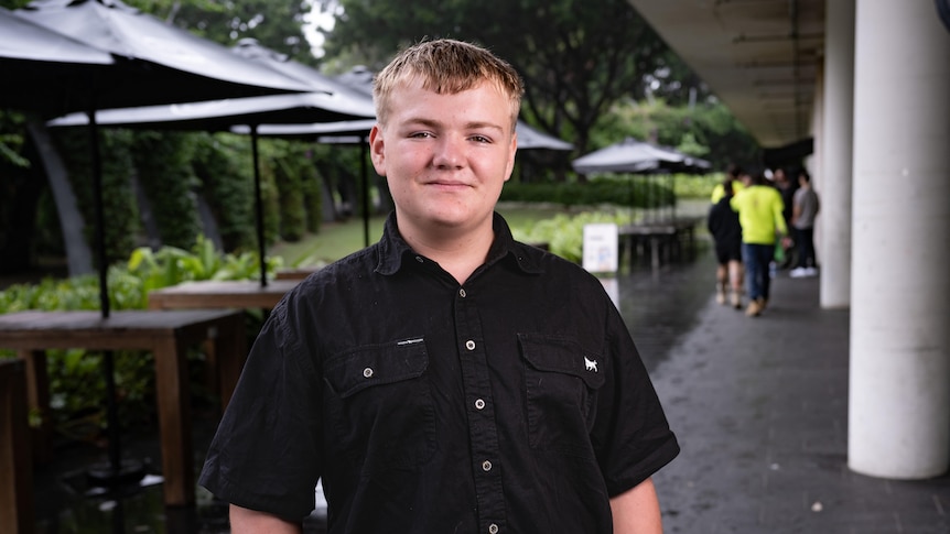 A smiling, fair-haired boy of 13, dressed in a dark shirt.