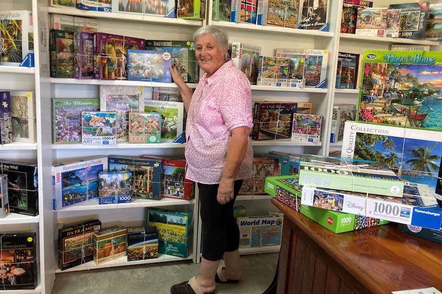 A woman stands in front of shelves lined with hundreds of puzzles in their boxes