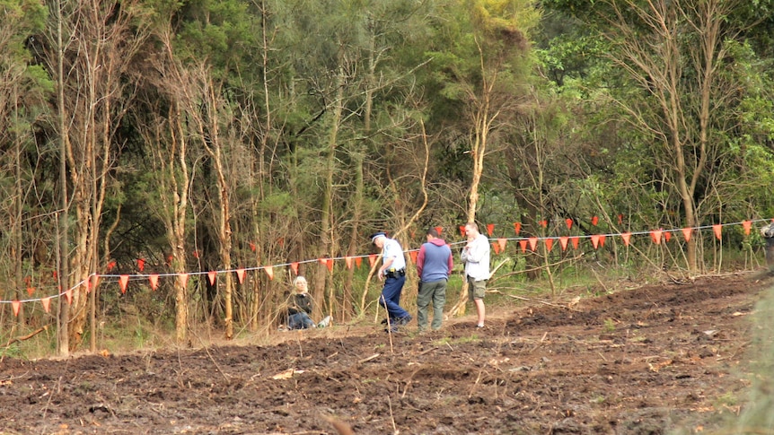 A woman sits behind felled bushland.