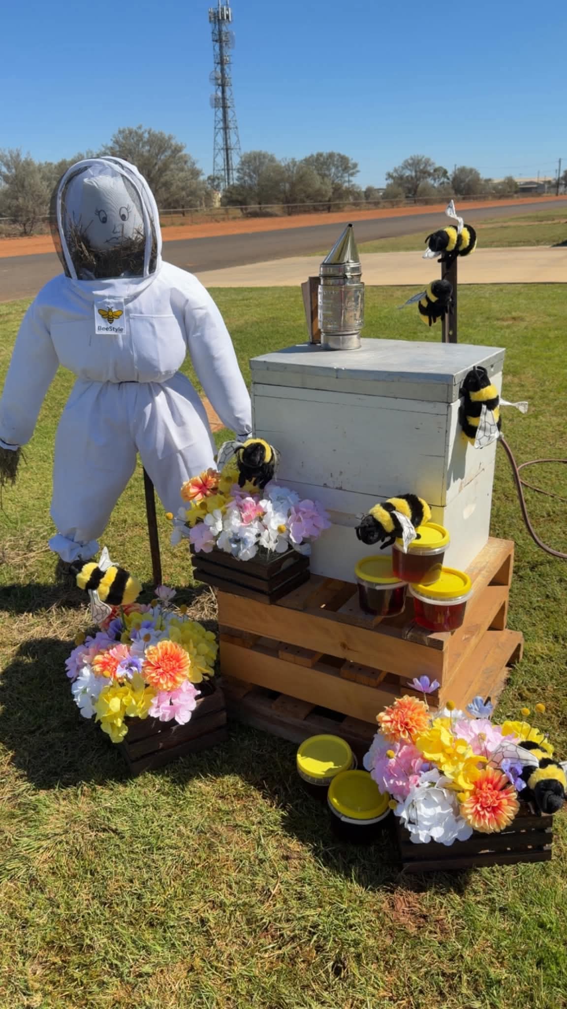 a scarecrow dressed as a beekeeper next to a prop hive