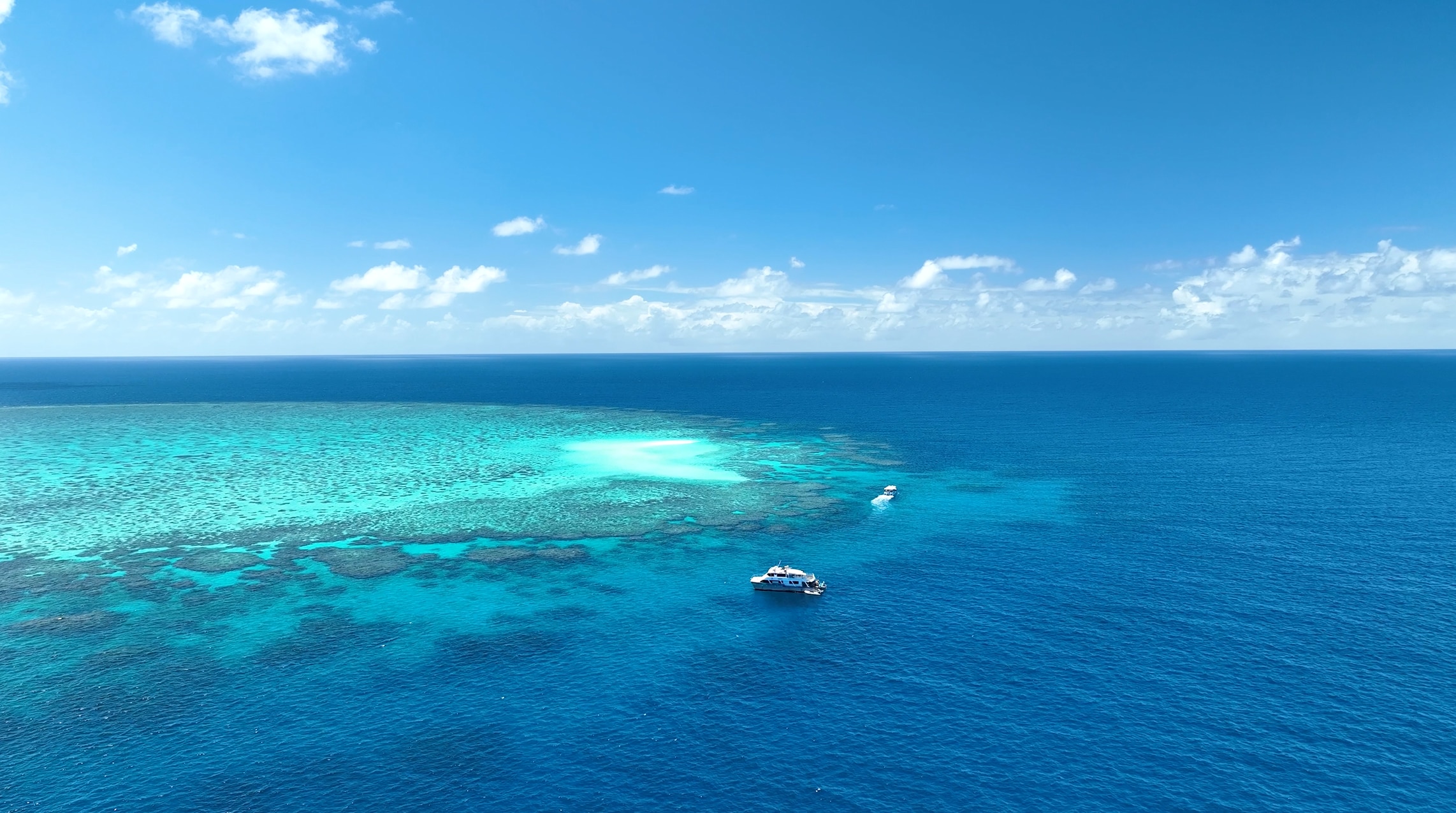 Un barco se acerca a un arrecife en un día deslumbrante, visto desde arriba.